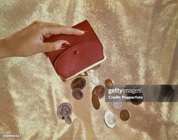 Posed studio shot of a woman's hand holding a red money purse with a selection of pre-decimal coins falling from the pocket, London, 18th November...