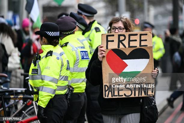 Pro-Palestinian supporter holds a placards as she walks past Met police officers while taking part in a "Day of Action for Palestine" demonstration...