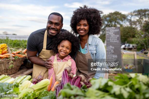 familia feliz vendiendo sus productos de cosecha propia en un mercado de agricultores - farm produce market fotografías e imágenes de stock