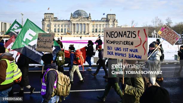 Participants march past the Reichstag building hosting Germany's parliament, with a banner reading "Compost Neo-Nazis - only the soil is brown here"...