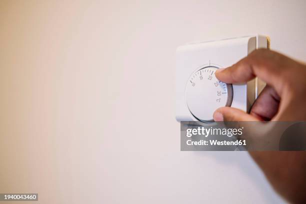 hand of man adjusting temperature of thermostat at home - thermostat stock pictures, royalty-free photos & images