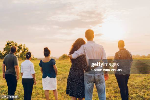 back view of happy young couple and their parents having fun in a public park during sunset time. - mom standing with son stock pictures, royalty-free photos & images
