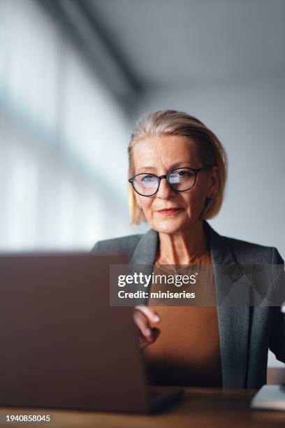 portrait of a serious senior business woman sitting at the table and using laptop computer - grey suit stock pictures, royalty-free photos & images