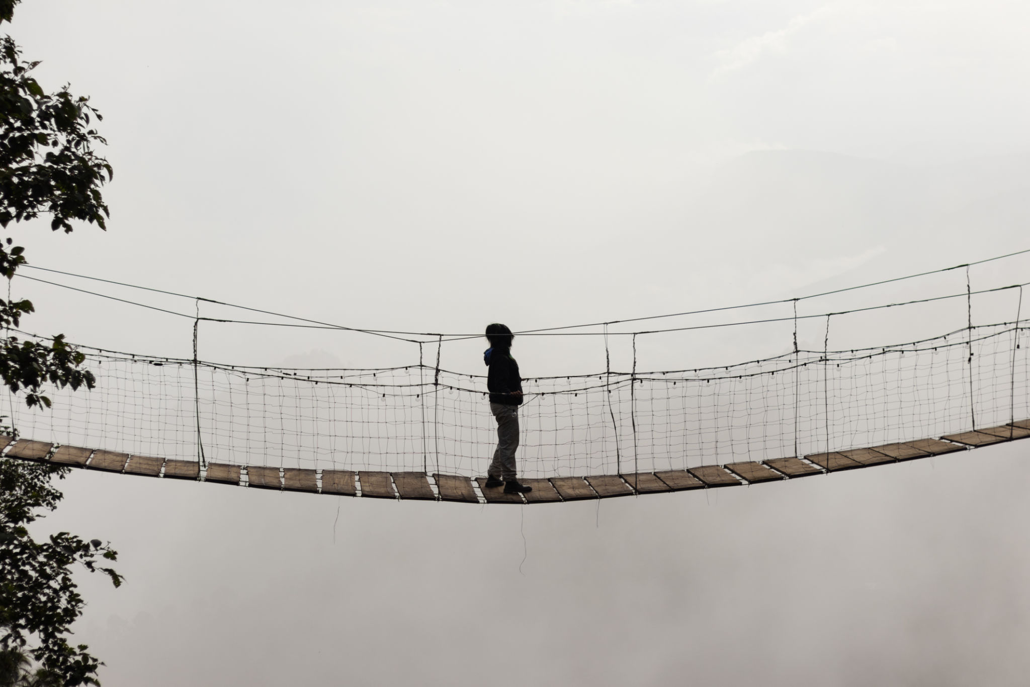Silhouette of a woman crossing a bridge contemplating the landscape of clouds and fog on her vacation alone Silhouette of a woman crossing a bridge contemplating the landscape of clouds and fog on her vacation alone