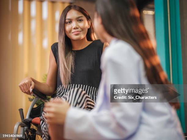 female doctor to consults with asian young transgender woman patients sitting on wheelchair while medical visit at clinic or nursing home - prevent illness stock pictures, royalty-free photos & images