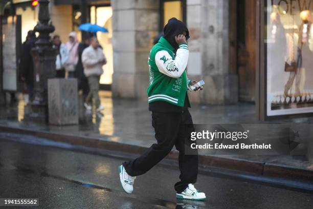 Guest wears sunglasses, a hoodie sweater, a green and white Louis Vuitton Teddy jacket, black pants, white sneakers, outside Bluemarble, during the...