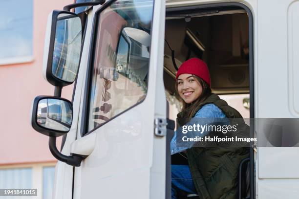 portrait of female professional truck driver sitting in a big truck, looking at camera and smiling. concept of women drivers, long distance trucking. - truck driver stock pictures, royalty-free photos & images