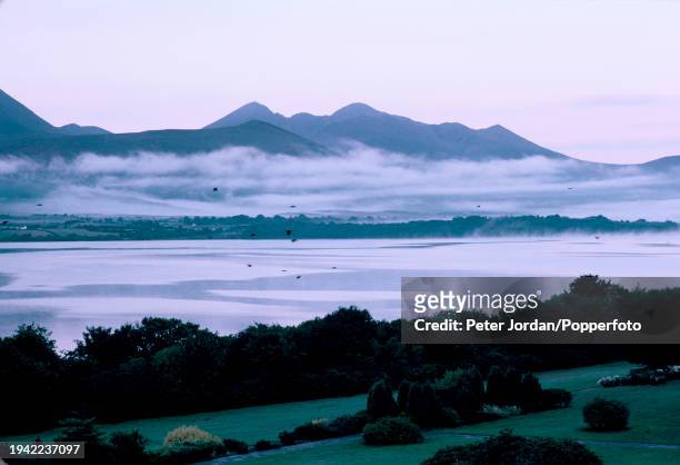 Birds fly over a sea inlet with mist and cloud lying over the water on the Dingle Peninsula in County Kerry in South West Ireland on 16th August 1984.