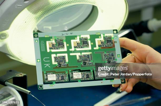 Female employee checks integrated circuit microchips mounted on a circuit board at the Panasonic company's phone production factory plant at Thatcham...