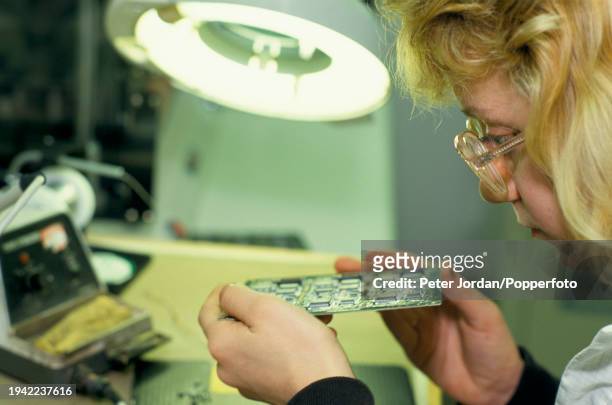 Female employee checks integrated circuit microchips mounted on a circuit board at the Panasonic company's phone production factory plant at Thatcham...