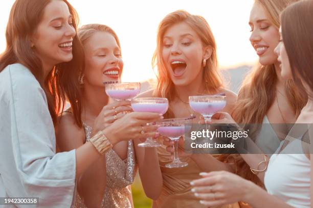 female friends wearing elegant dresses drinking lavender drinks outdoors at sunset - long dress party stock pictures, royalty-free photos & images