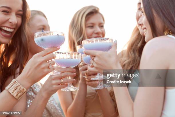 female friends wearing elegant dresses drinking lavender drinks outdoors at sunset - bachelorette stock pictures, royalty-free photos & images