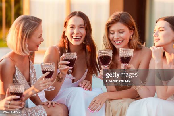 female friends wearing elegant dresses drinking wine outdoors at sunset - women in long dress stock pictures, royalty-free photos & images