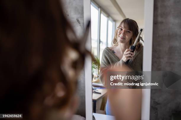 young woman using a hair curler at home - krulspelden stockfoto's en -beelden