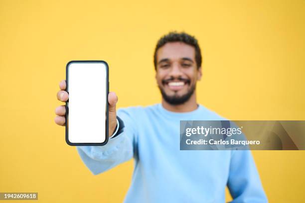 portrait of a young latin american man showing a blank screen phone to the camera for advertisement. - homens de idade mediana imagens e fotografias de stock