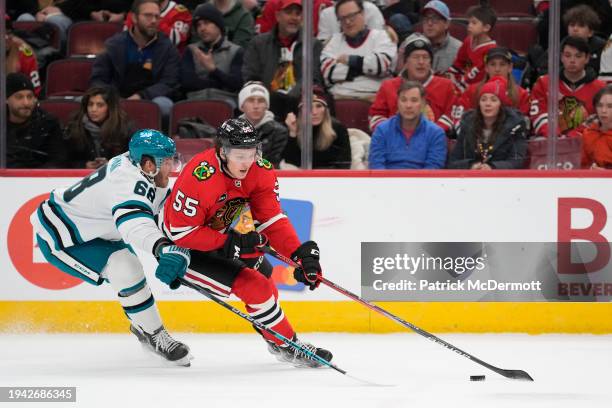 Kevin Korchinski of the Chicago Blackhawks skates with the puck against Mike Hoffman of the San Jose Sharks during the first period at the United...