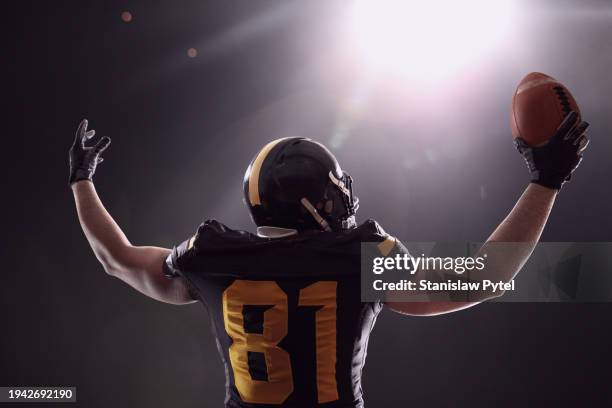 football player celebrating, rasing hands, holding ball against stadium light and dark background - team sport stock pictures, royalty-free photos & images