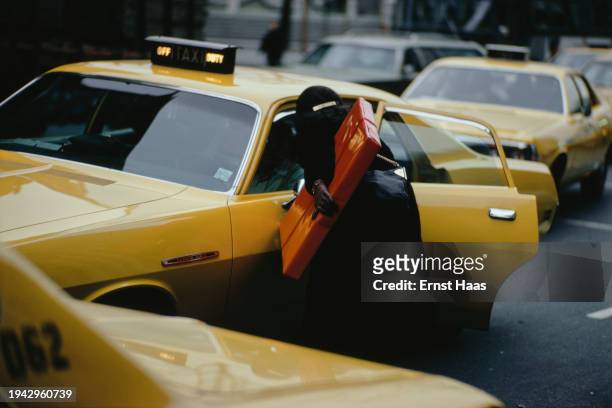 Woman carrying a gift-wrapped parcel stops a Dodge taxi during the Christmas shopping season in New York City, circa 1975.