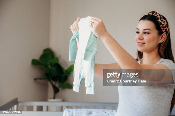 an expectant mother folds baby clothing in the nursery, eagerly anticipating the arrival of her baby. - babygro stock pictures, royalty-free photos & images