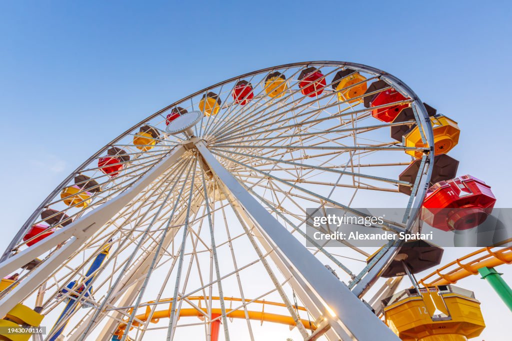 Low angle view of multi-coloured vibrant ferris wheel against blue sky