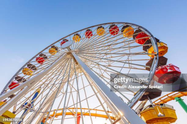 low angle view of multi-coloured vibrant ferris wheel against blue sky - amusement park foto e immagini stock