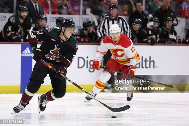 Travis Dermott of the Arizona Coyotes skates with the puck ahead of Yegor Sharangovich of the Calgary Flames during the first period of the NHL game...