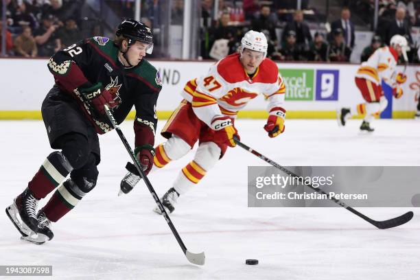 Logan Cooley of the Arizona Coyotes skates with the puck ahead of Connor Zary of the Calgary Flames during the first period of the NHL game at...