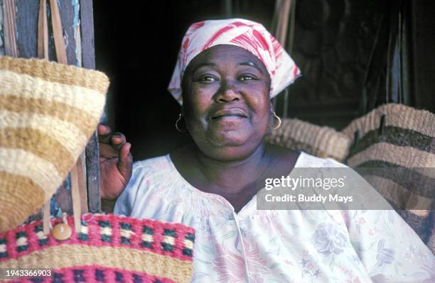 Black woman sells straw bags and hats to visitors and other tourists at an open, outdoor market in downtown Nassau, Bahamas, 1986. .