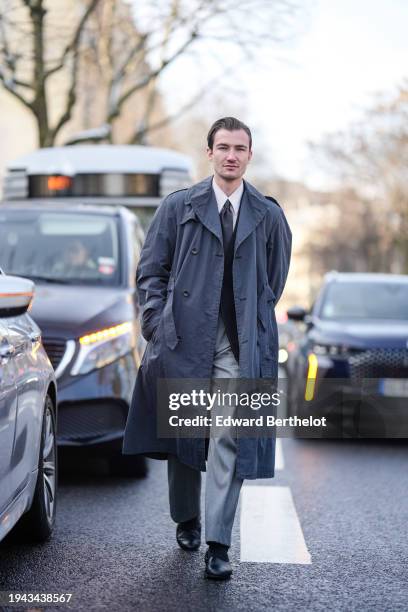 Brett Staniland wears a gray trench coat, a white shirt, a tie, gray suit pants, black socks, leather shoes, outside Issey Miyake, during the...