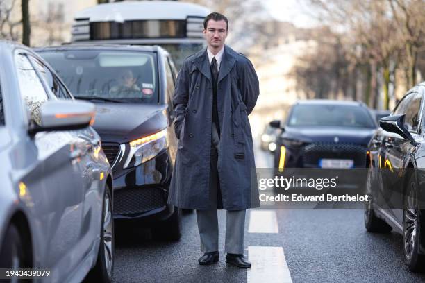 Brett Staniland wears a gray trench coat, a white shirt, a tie, gray suit pants, black socks, leather shoes, outside Issey Miyake, during the...