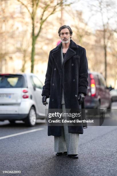 Richard Biedul wears a necklace, a gray suit, a black long fluffy winter coat, black leather gloves, outside Issey Miyake, during the Menswear...