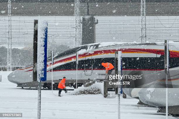 Railway workers clear snow from a bullet train in Nanchang West Railway Station in Nanchang, in central China's Jiangxi province on January 22, 2024....