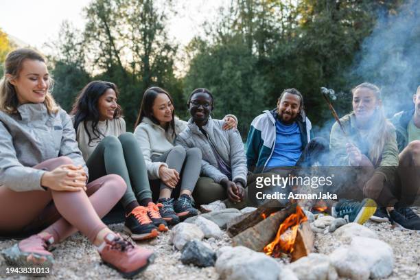 diverse group of friends enjoying a campfire outdoors - reünie sociaal stockfoto's en -beelden