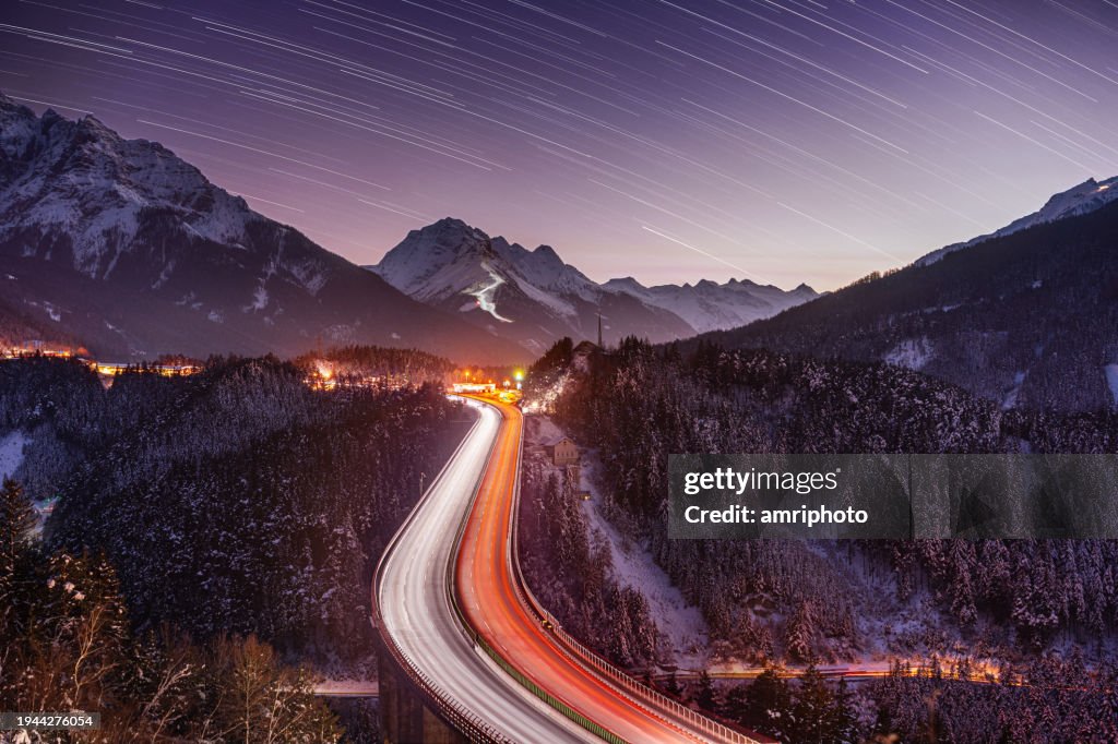 Winter night with star and ligh trails, motorway on bridge in mountains