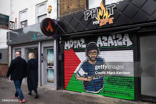 Members of the public pass artwork featuring an image of Palestinian journalist Motaz Azaiza on a Palestinian flag painted on a shop blind in Tower...