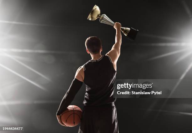 Basketball Player Holding Big Trophy Above Head Celebrating Vistory Holding Ball Against Black Background High-Res Stock Photo