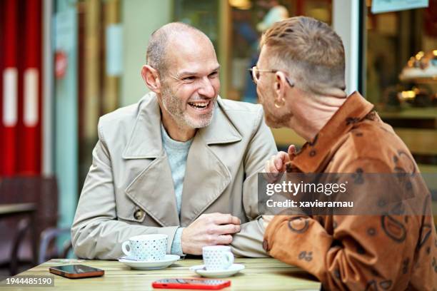 smiling gay men enjoying outdoor coffee date - close to stock pictures, royalty-free photos & images