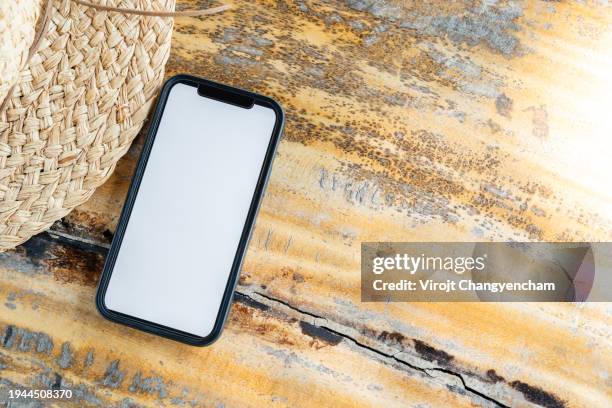 a white-screened smartphone placed on a table with a woven hat - travel essentials stock pictures, royalty-free photos & images