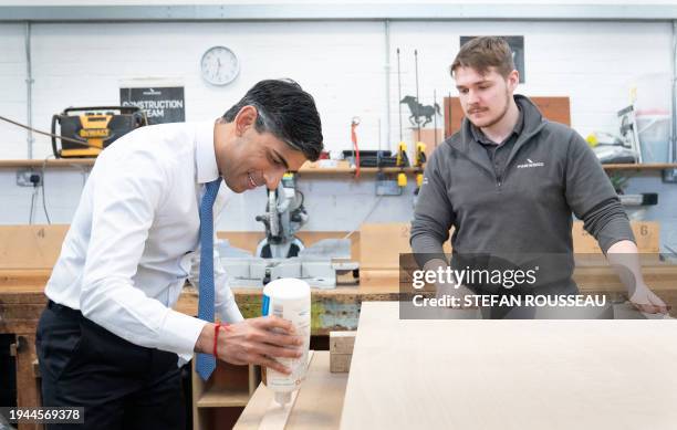 Britain's Prime Minister Rishi Sunak uses glue as he helps to make a wooden door with carpentry apprentice Adam Jellis during a visit to Pinewood...
