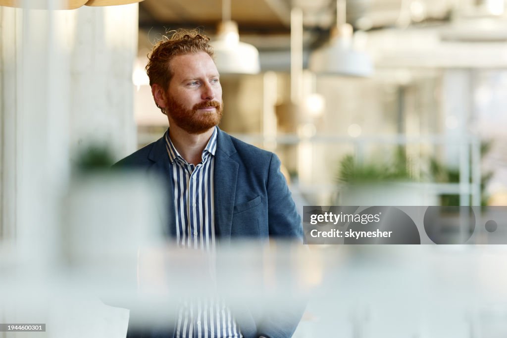 Lächelnder rothaariger Geschäftsmann, der im Büro tagträumt.