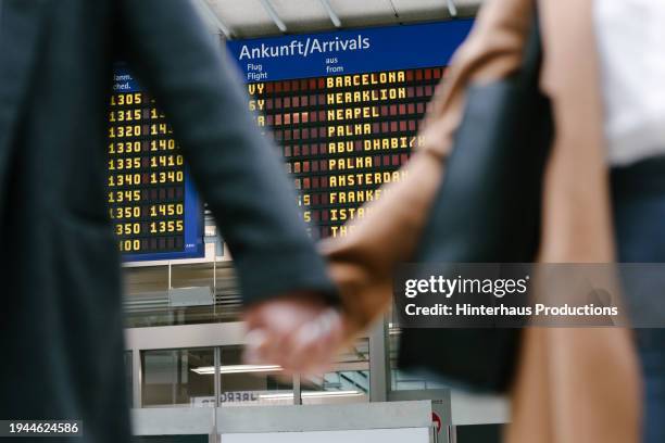 view of airport terminal flight board through couples arms - fokus-auf-den-hintergrund stock-fotos und bilder