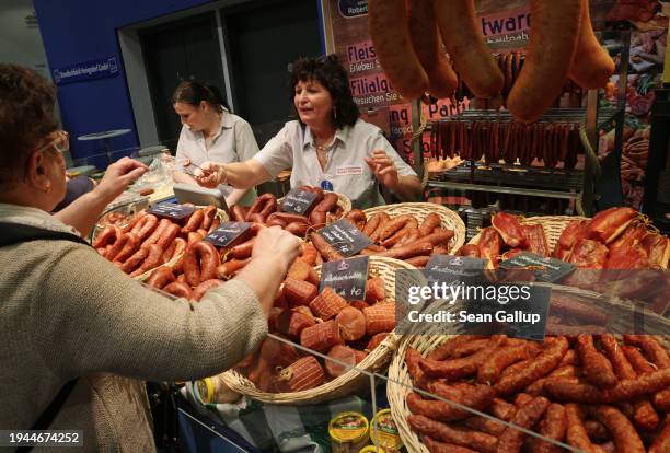 Stand hostess gives a visitor a sample of a sausage at the stand of a meat products manufacturer at the Green Week agricultural trade fair on its...