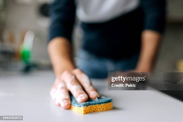 primo piano di un uomo irriconoscibile che pulisce il bancone della cucina con una spugna - spugna per le pulizie foto e immagini stock