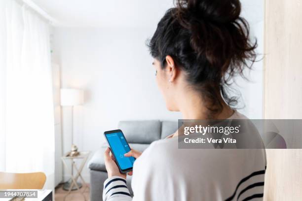 rear view of woman controlling with smartphone domestic lamp at living room - mensagem com foto imagens e fotografias de stock