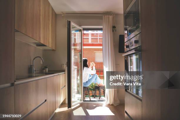 spanish woman sitting at home balcony drinking coffee looking through the window. - neighbors balcony stock pictures, royalty-free photos & images