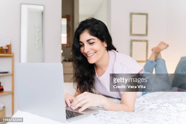 spanish woman smiling using technology working at confortable bedroom - confortable imagens e fotografias de stock