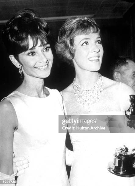 British actor Julie Andrews holds her Oscar while standing with Belgian born actor Audrey Hepburn at the Academy Awards ceremonies in Santa Monica,...