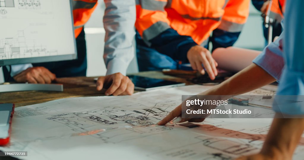 Closeup of team of industrial engineers meeting analyze machinery blueprints consult project on table in manufacturing factory. Working in manufacturing plant or production plant.