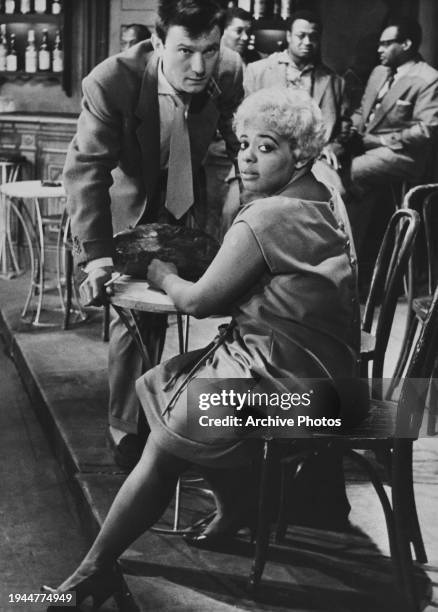 Lithuanian-born British actor Laurence Harvey stands, leaning on a table, as American singer and actress Bertice Reading sits at the table during a...