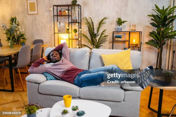 young man relaxing on the sofa at home at night - relaxing on sofa stock pictures, royalty-free photos & images